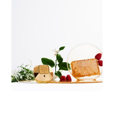 Frasco de perfume dourado com flores, framboesas e favo de mel