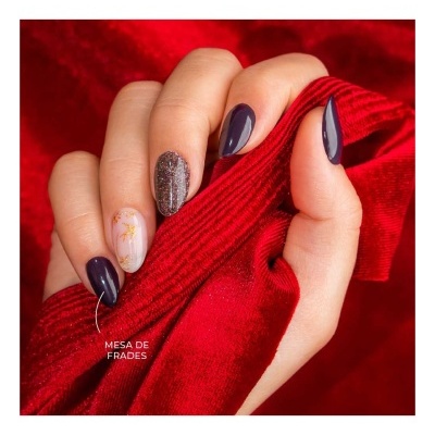 Unhas decoradas em tons roxos, glitter e branco com dourado, mão segura tecido vermelho aveludado