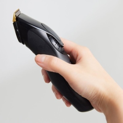 Máquina de cortar cabelo preta com lâmina dourada segurada por uma mão