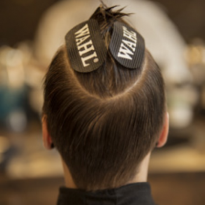 Pessoa com cabelo curto e etiquetas WAHL no topo, num salão de cabeleireiro