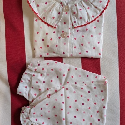 Conjunto de pijama infantil branco com bolas rosa e vermelho sobre tecido listrado vermelho e branco.