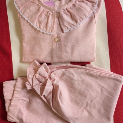 Pijama rosa claro com pontos brancos e gola rodada sobre cadeira listrada vermelha e branca