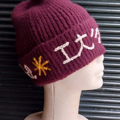 Gorro bordeaux com bordados branco e amarelo numa cabeça de manequim branca