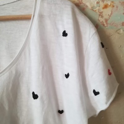 Camisola branca com corações pretos e vermelho em manga, pendurada num cabide