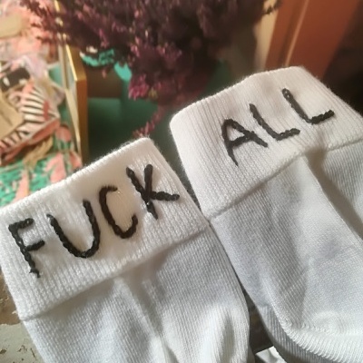 Meias brancas com texto preto bordado e flores roxas ao fundo