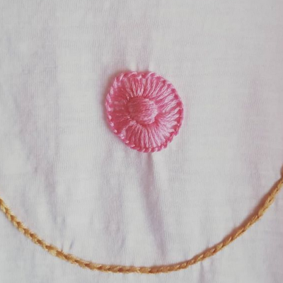 Tecido branco com bordado rosa circular e linha castanha fina bordada.