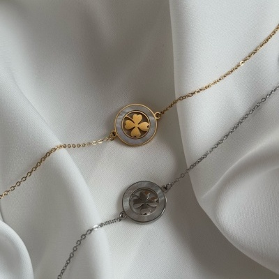 Duas pulseiras com trevos, uma dourada e outra prateada, sobre tecido branco