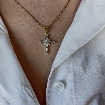 Colar dourado com pendente de cruz decorada com pedras ao pescoço de pessoa com camisa branca