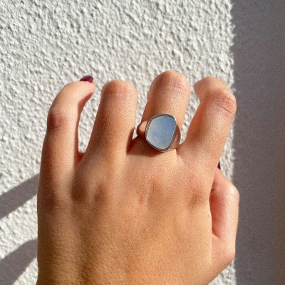 Anel de prata com pedra azul claro em mão contra parede branca texturada