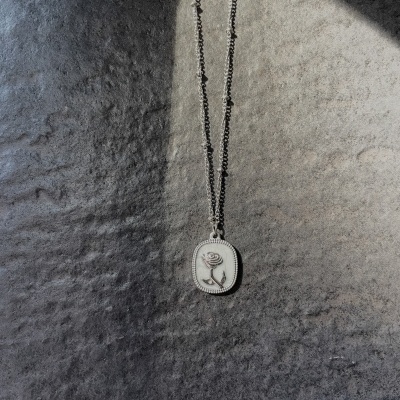 Colar prateado com pendente de rosa em relevo sobre fundo cinza texturizado