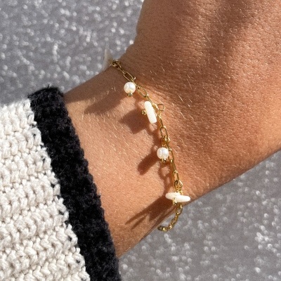 Pulseira dourada com pérolas e pedras brancas no pulso