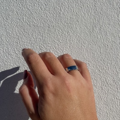 Mão com anel prateado contra parede branca texturizada