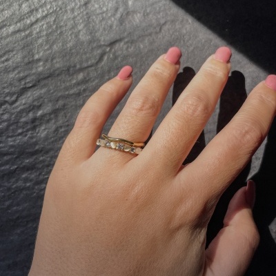 Mão com anéis dourados e unhas rosa sobre superfície cinza