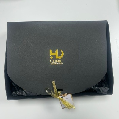 Caixa preta com logo HD CLINIC dourada e fecho de fita dourada