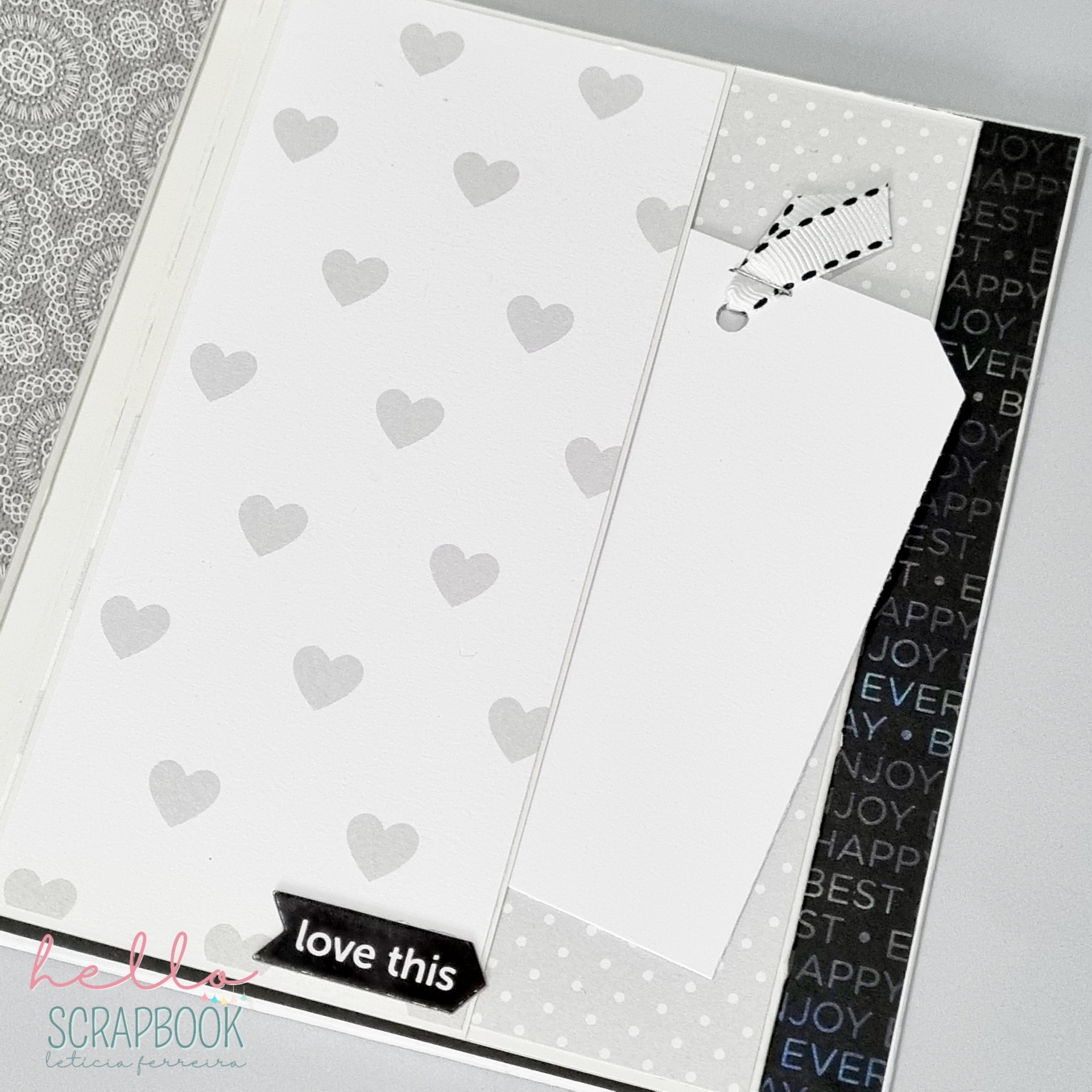 Página de scrapbook com papel decorado com corações, marcador de papel e fita preta com texto 'love this'