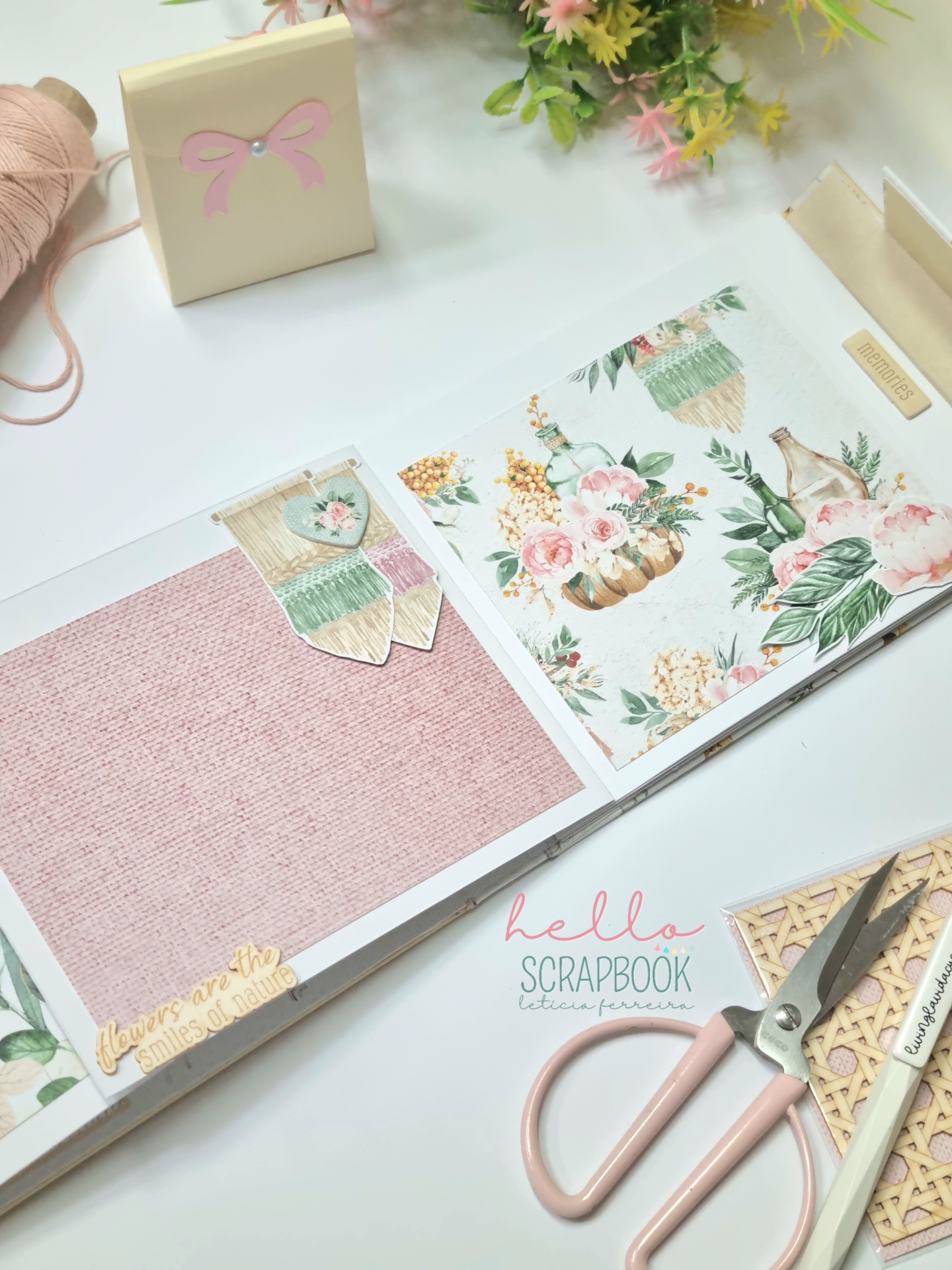 Suporte de scrapbook aberto com páginas decoradas em mesa branca com ferramentas de artesanato.