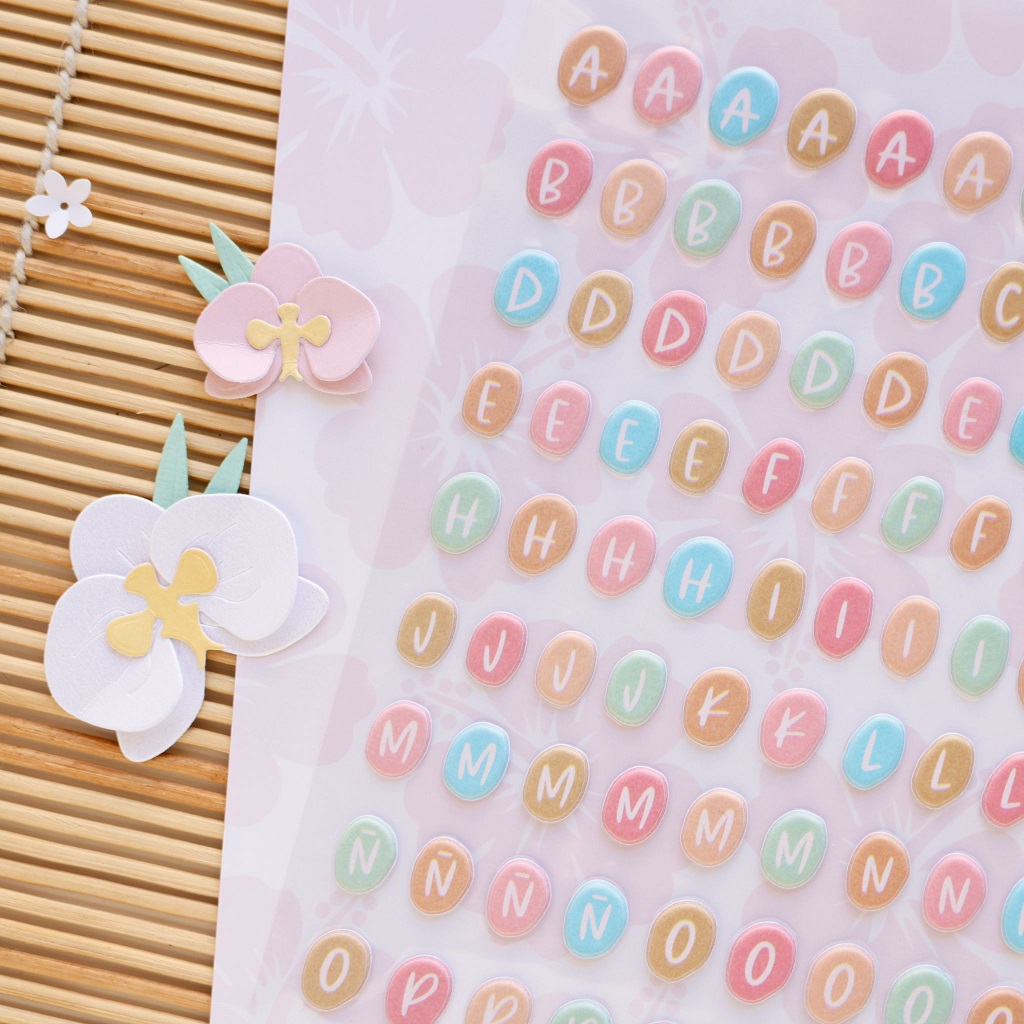 Autocolantes de letras coloridas com flores de orquídea de papel sobre superfície de madeira clara