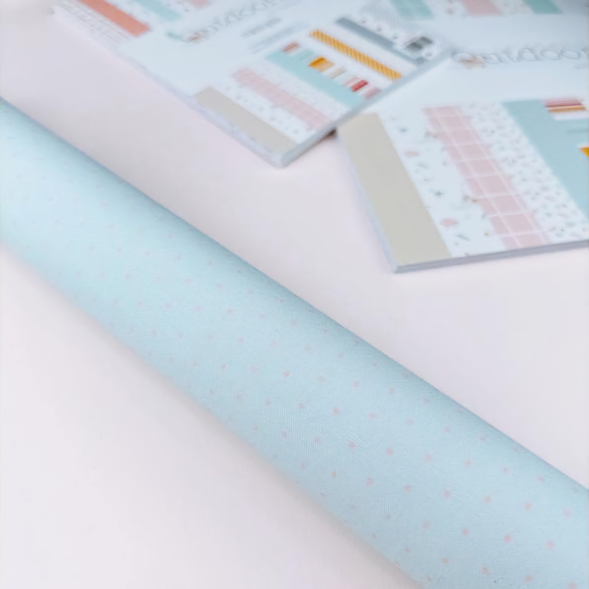 Rolo de papel azul claro com estrelas rosas ao lado de folhas de amostras coloridas sobre mesa branca
