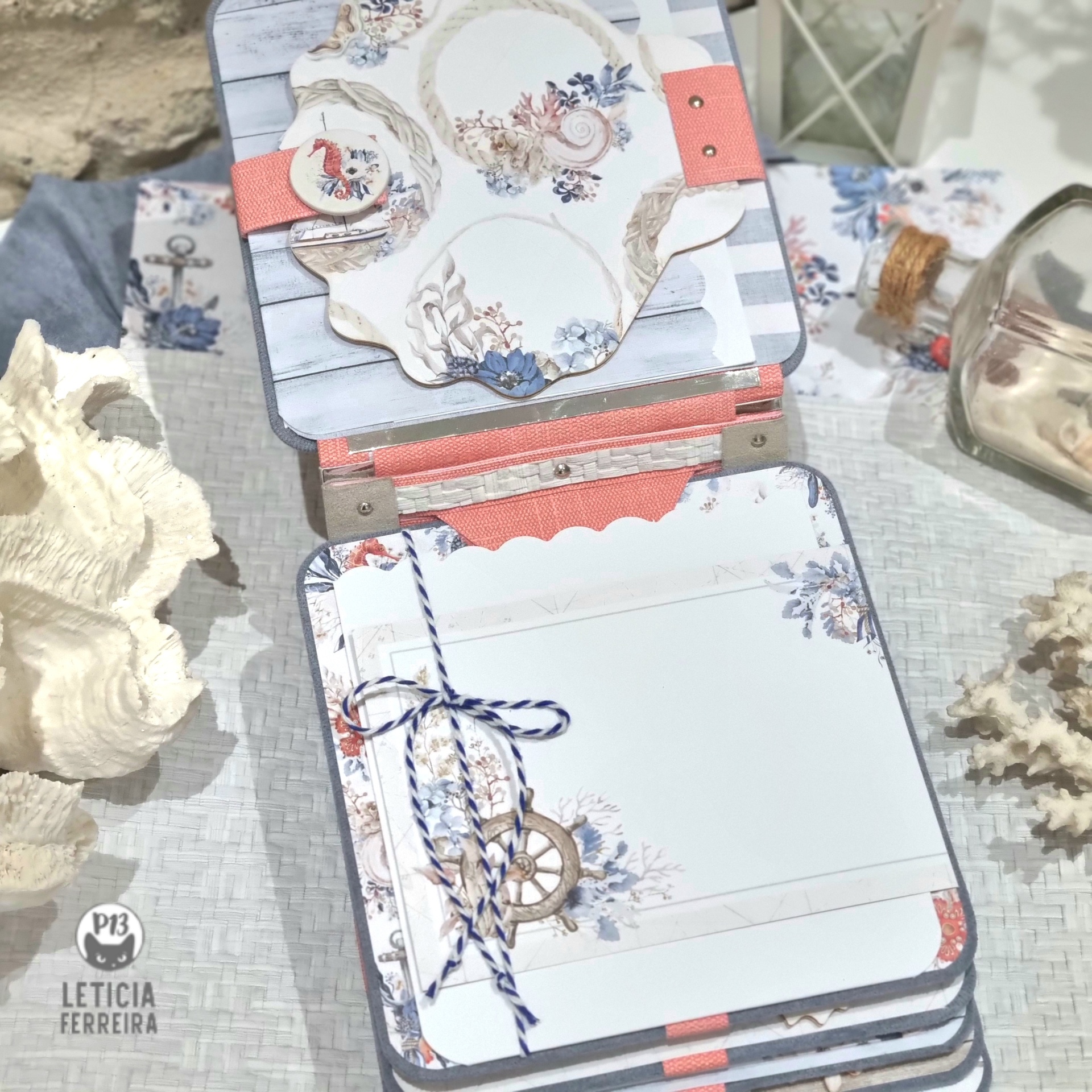 Produto artesanal de papel com tema náutico em tons azul, branco e salmão com corda e leme, sobre superfície clara com conchas