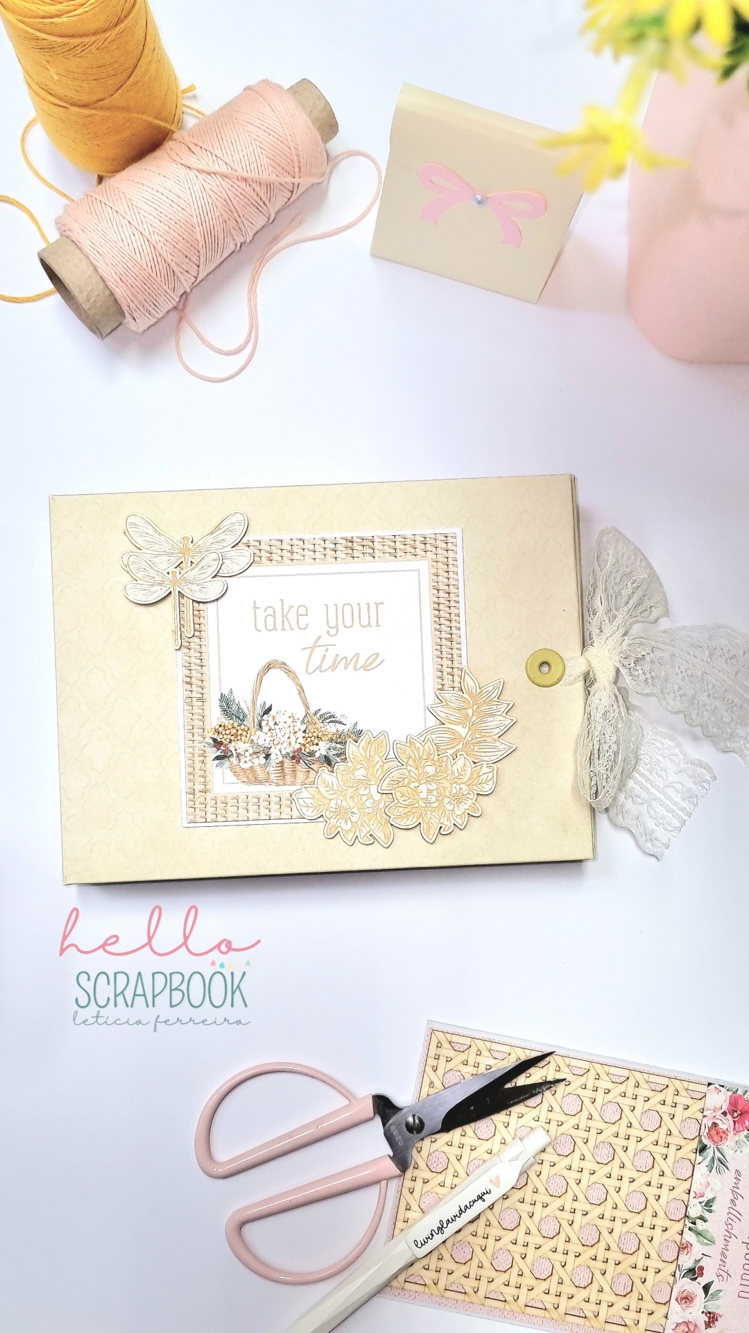 Álbum de scrapbook decorado com flores e borboleta em bege com fita de renda, tesoura rosa, cartão e rolos de fio