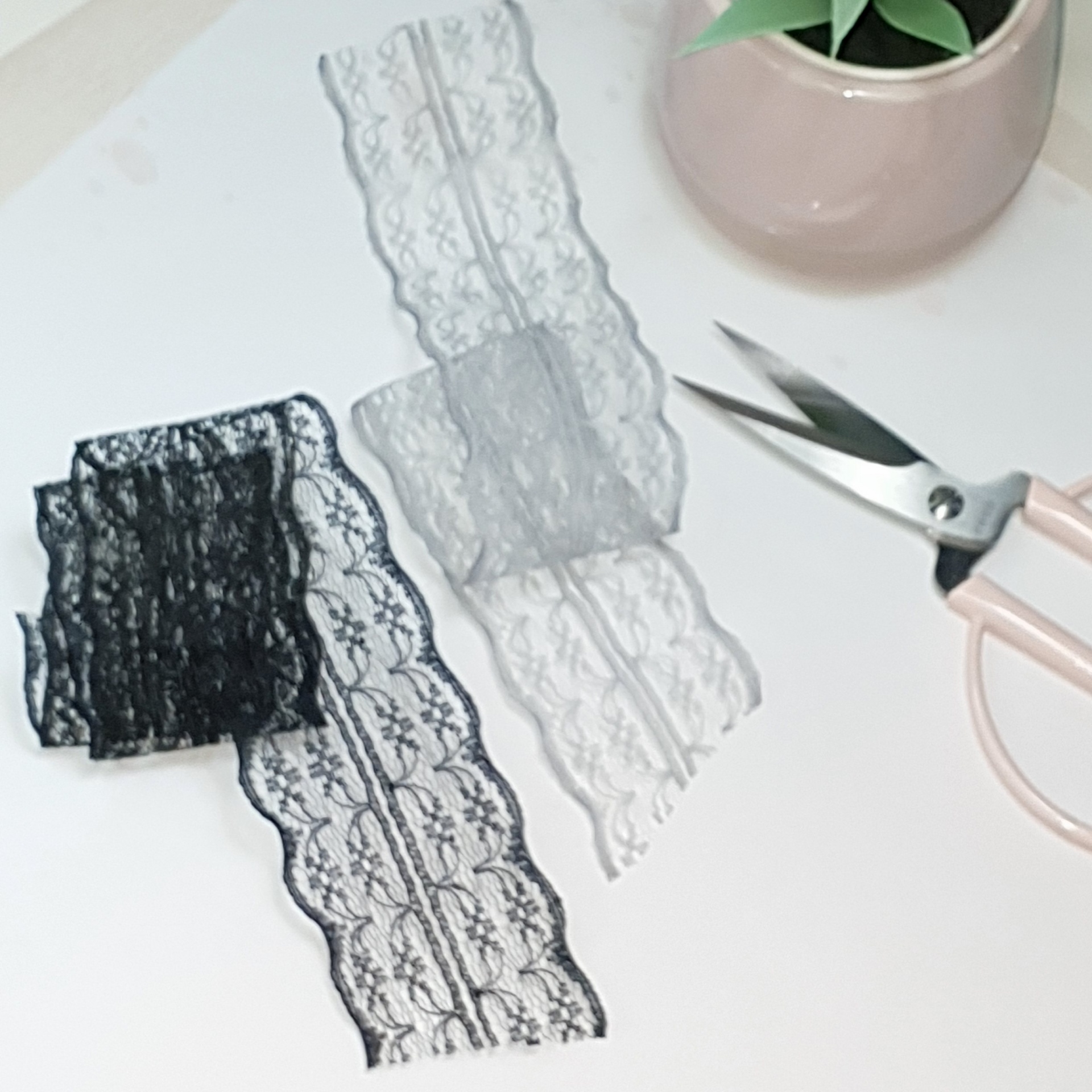 Fitas de renda preta e branca com tesoura e vaso com planta