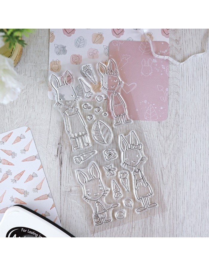 Conjunto de carimbos transparentes de coelhos e itens, sobre mesa de madeira clara com papéis decorativos de fundo.