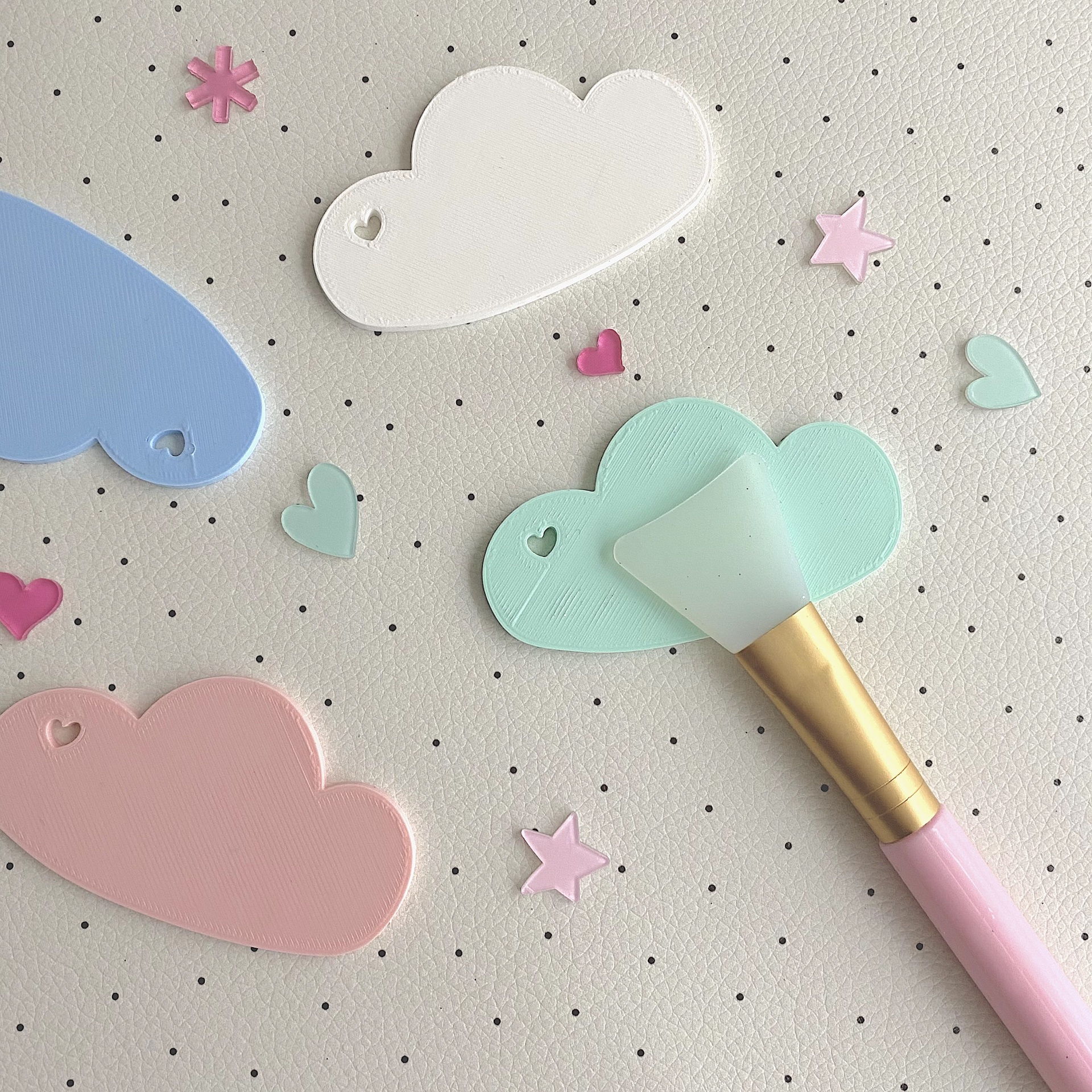 Espátulas em forma de nuvem de silicone coloridas e pincel de maquiagem rosa sobre superfície pontilhada