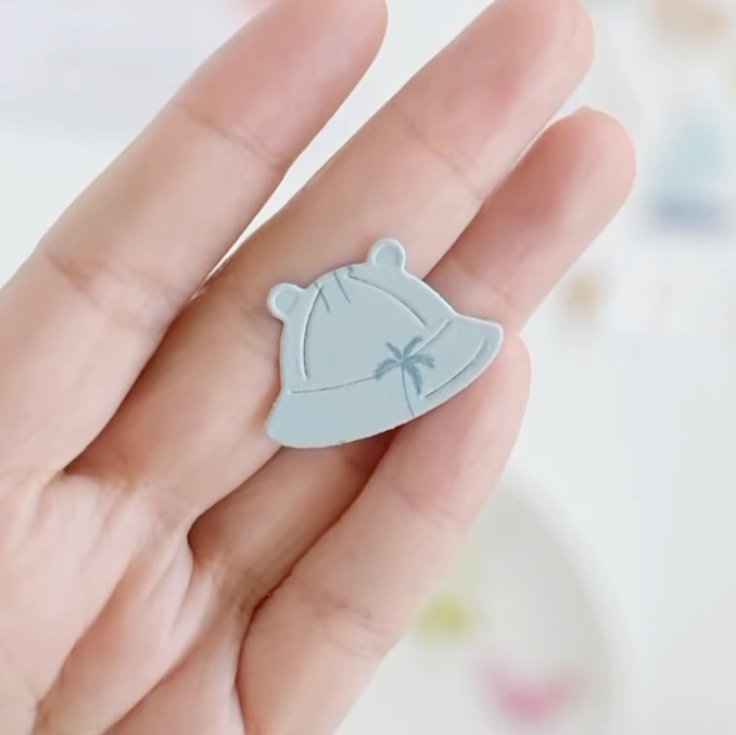 Figura decorativa cinza em forma de chapéu com desenho de aranha, segurada por uma mão