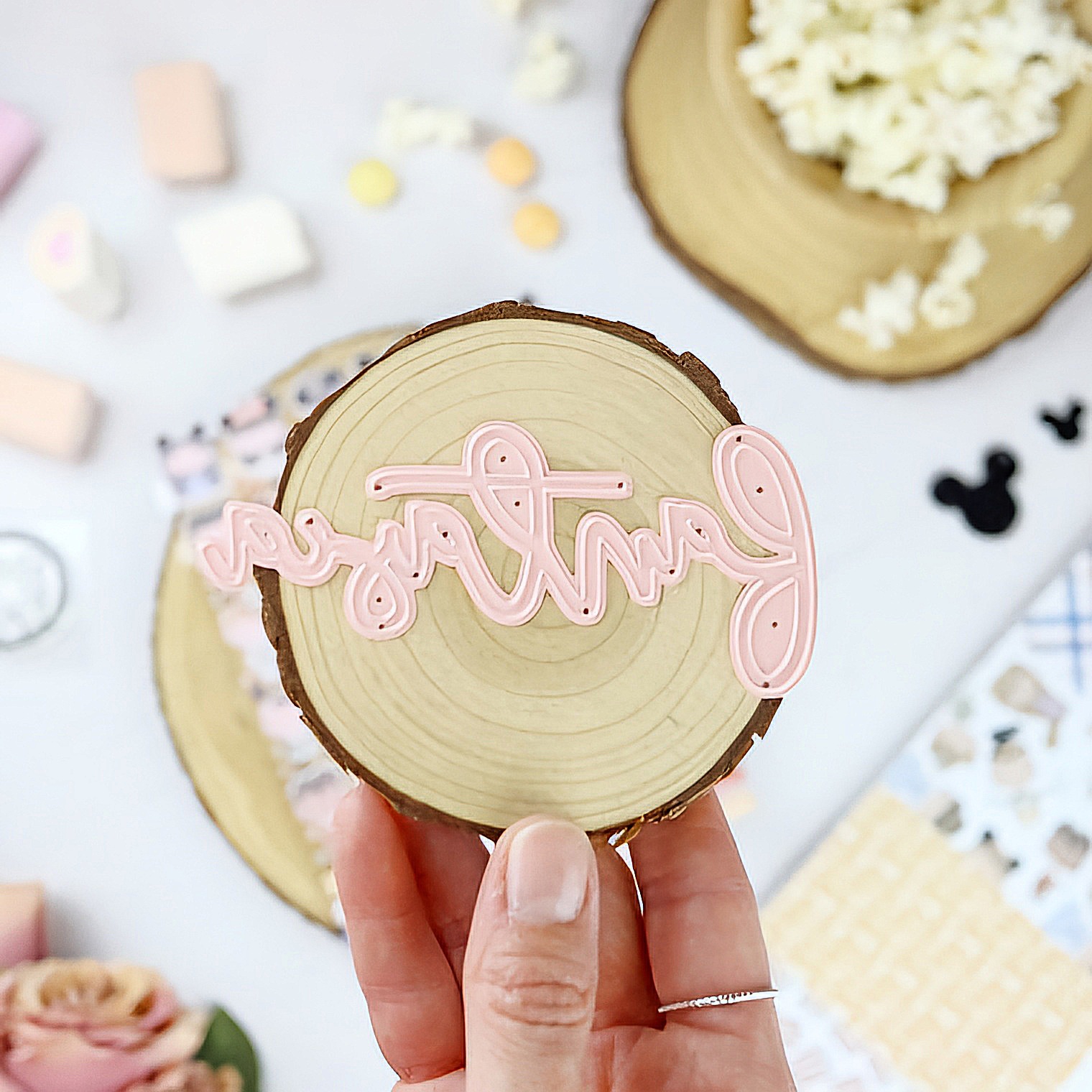 Disco de madeira com palavra rosa 'partners' em relevo, segurado por mão, fundo desfocado com marshmallows e pipoca.