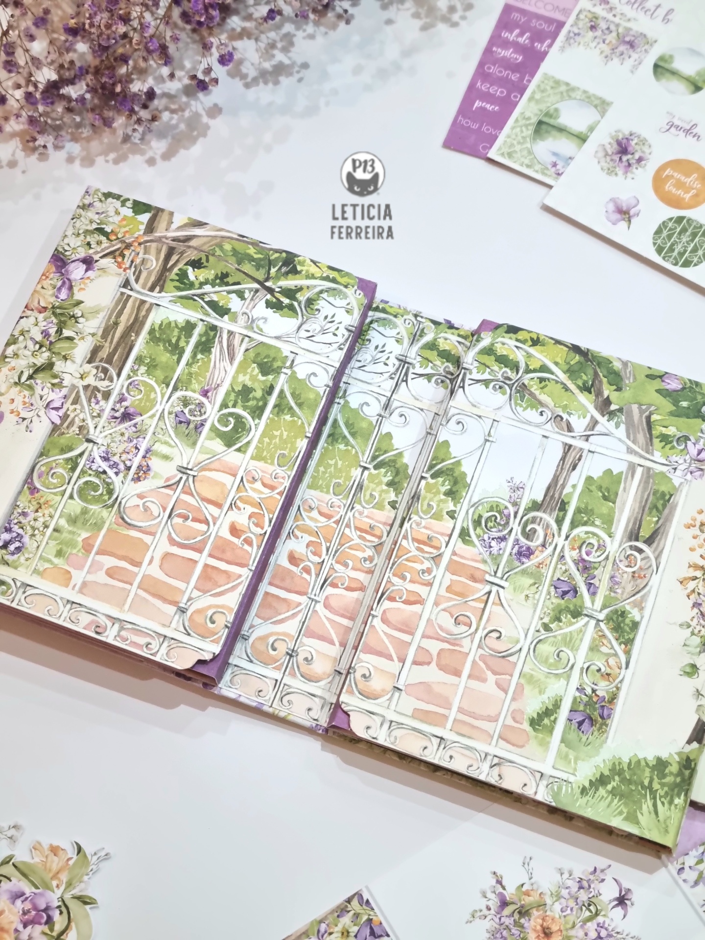 Livro ilustrado aberto mostrando portão de ferro branco com caminho de tijolos e vegetação