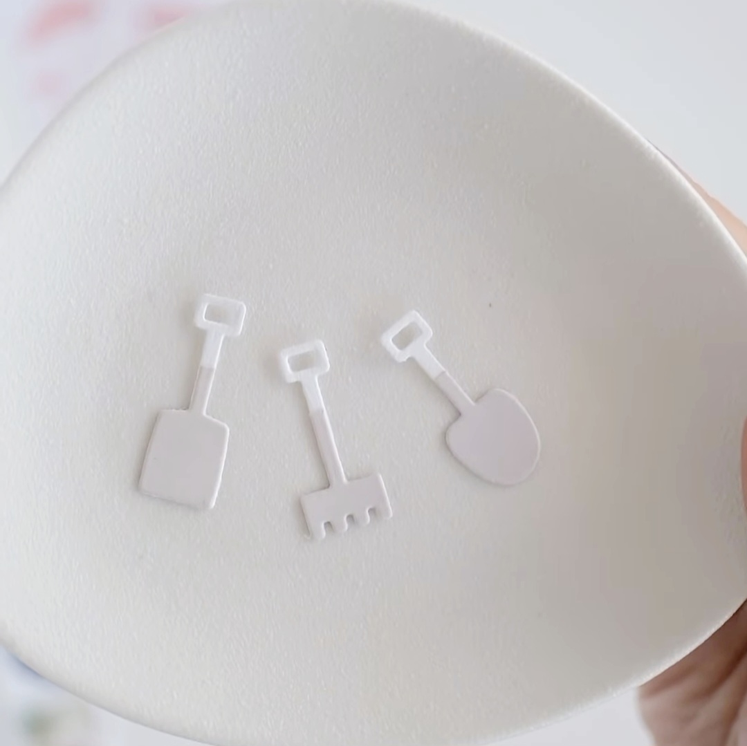 Placa branca com três mini ícones de ferramentas de jardinagem em relevo