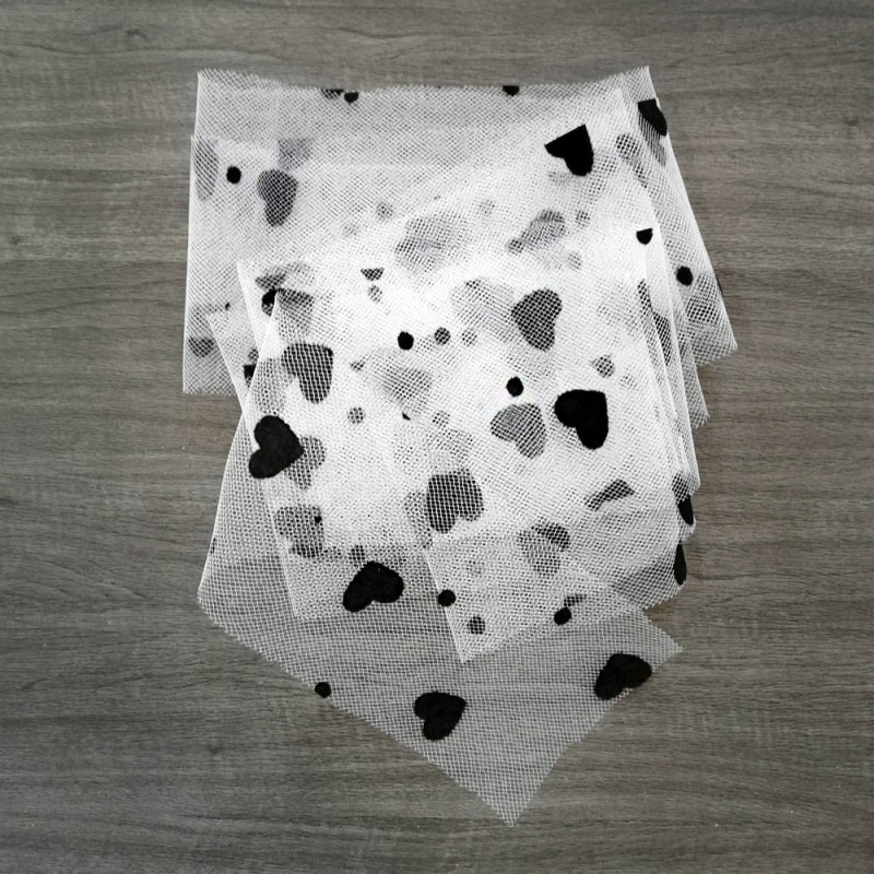 Tecido branco com padrão de corações pretos e cinzentos sobre mesa de madeira clara