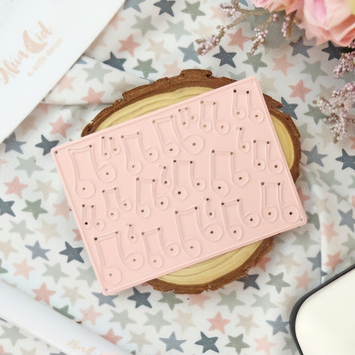 Bloco organizador cor-de-rosa sobre base de madeira em pano com estrelas multicoloridas.