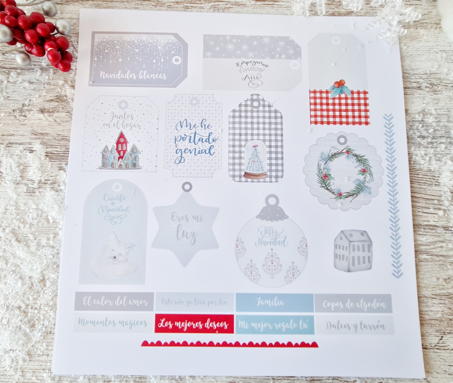 Folha de adesivos de Natal com frases e desenhos em tons cinza, azul, vermelho e branco sobre madeira clara