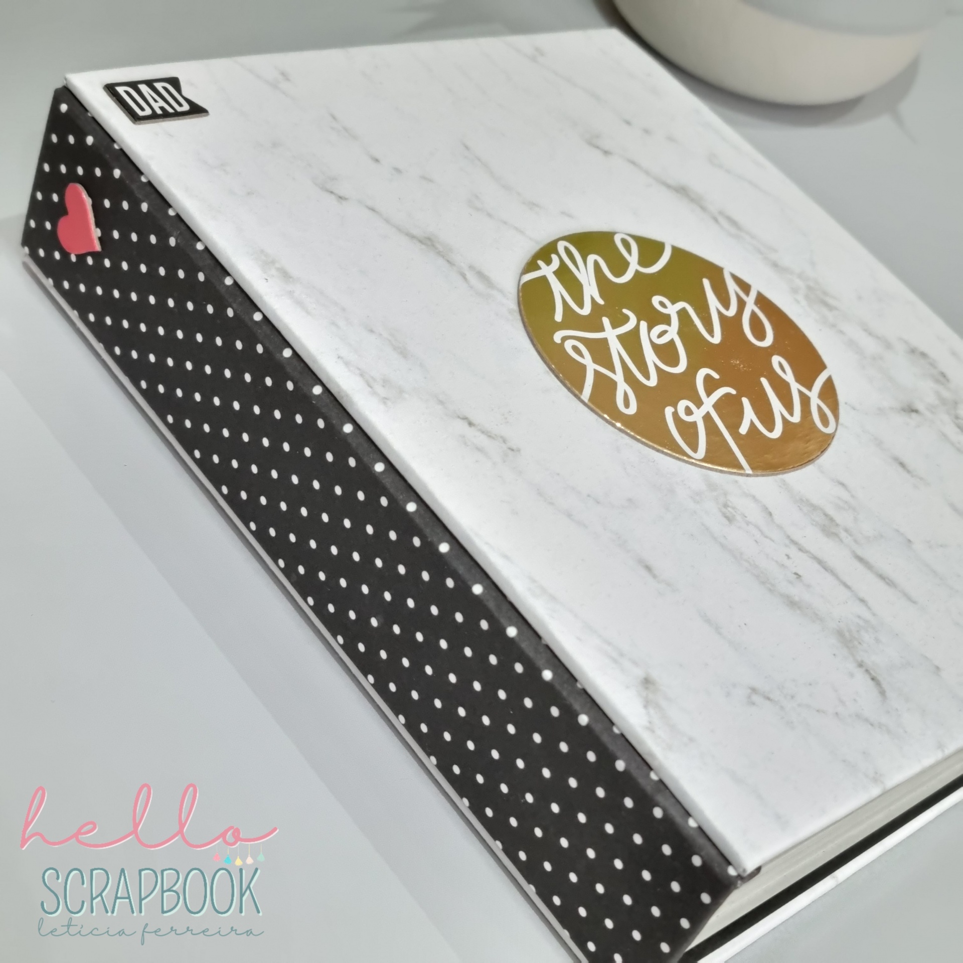 Álbum fotográfico com capa de mármore branco detalhes a preto com bolinhas brancas e etiqueta DAD