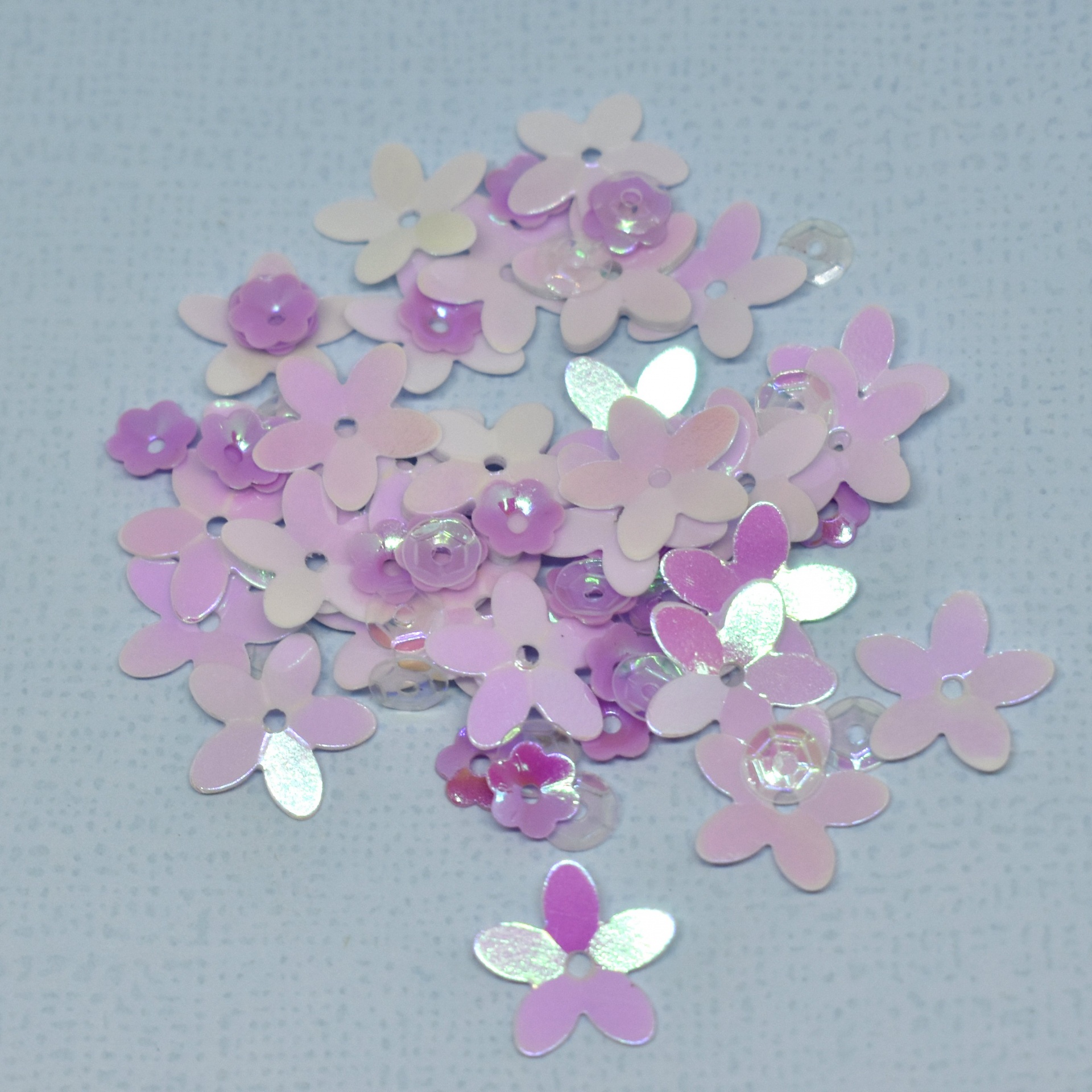 Lantejoulas florais rosas e lilás sobre superfície azul clara