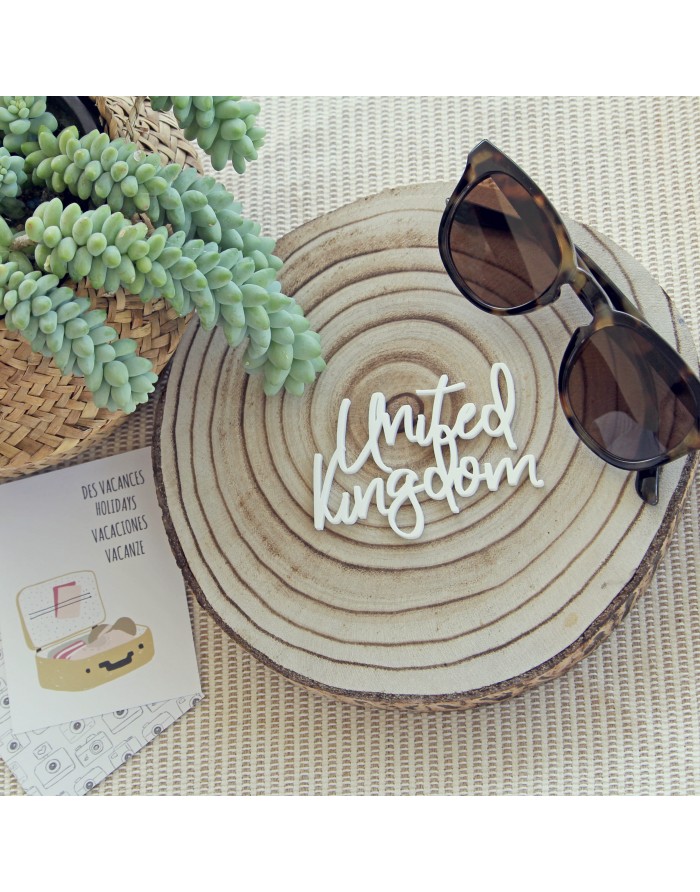 Óculos de sol castanhos escuros sobre base de madeira redonda com planta verde e cartão de férias