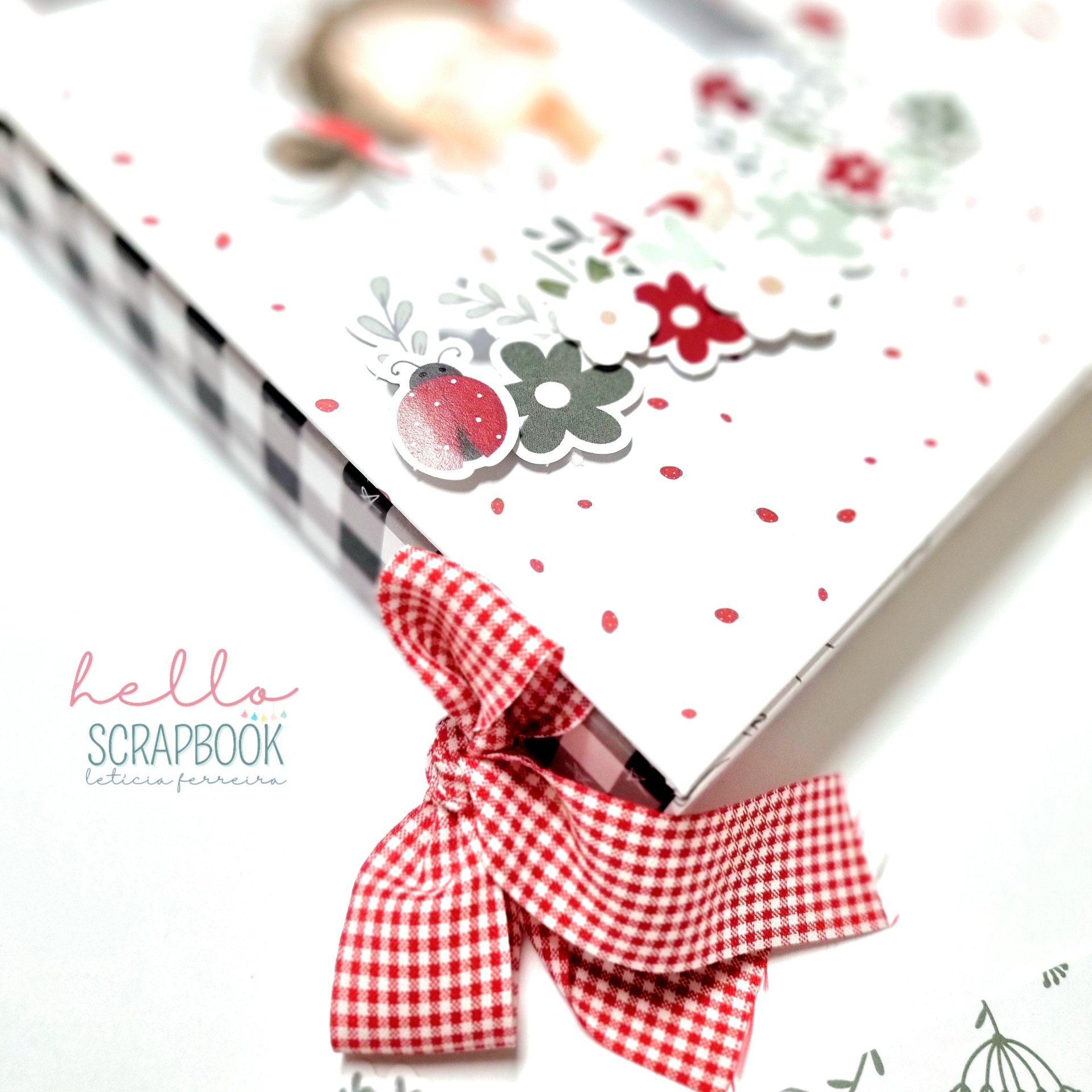 Livro de scrapbook com capa decorada e laço vermelho e branco aos quadrados