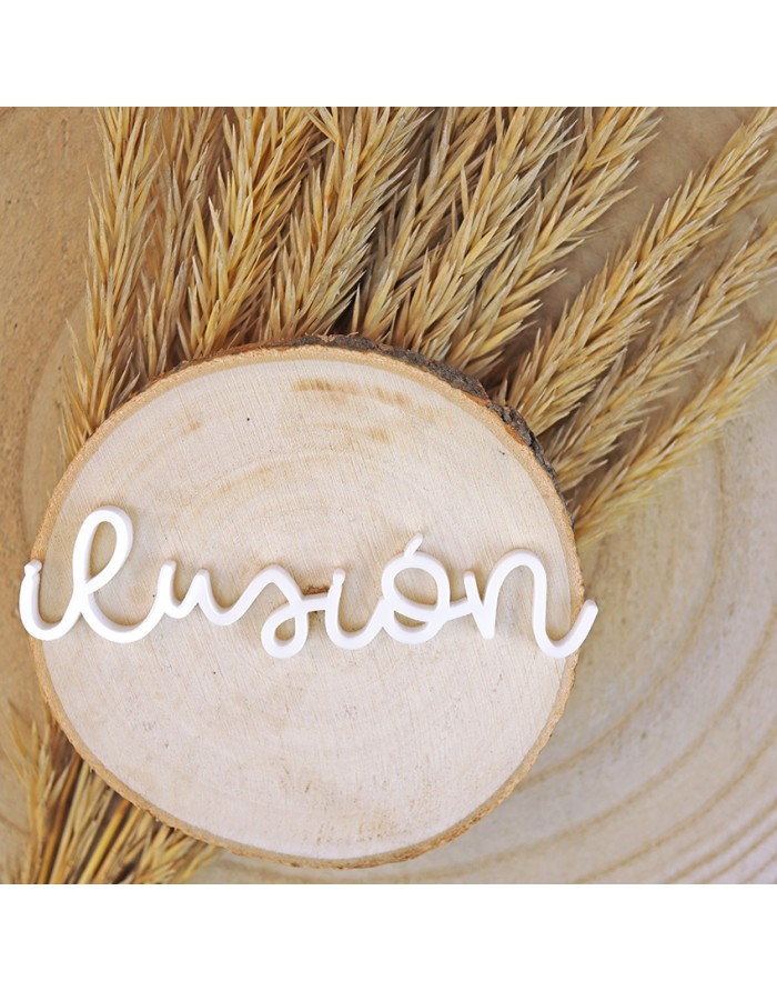 Palavra 'ilusión' em letras brancas sobre tábua redonda de madeira com capim seco ao fundo