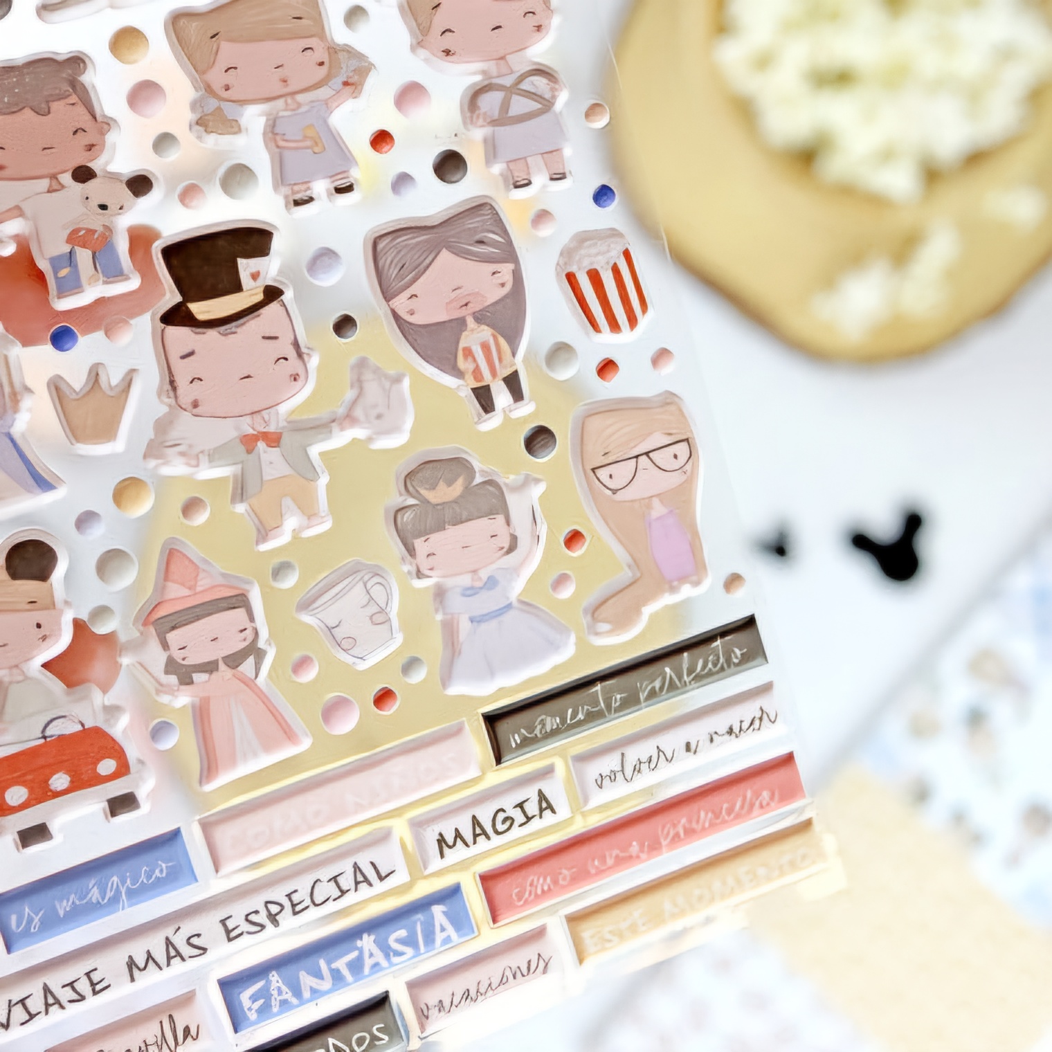 Adesivos coloridos com personagens e etiquetas coloridas com texto em espanhol ao lado de um tapete bege e textura branca