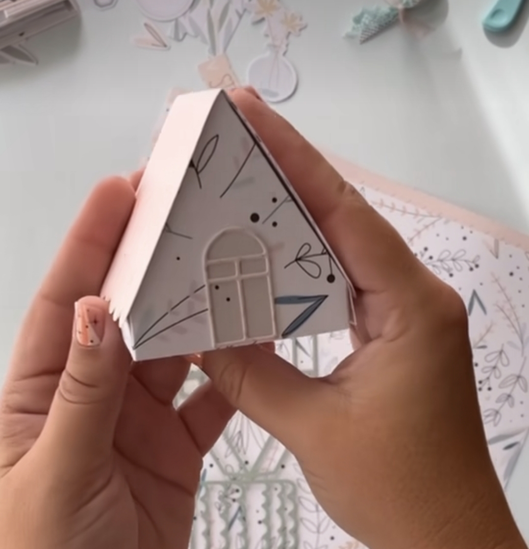 Miniatura de casa de papel branca com desenhos pretos e triângulo azul nas mãos