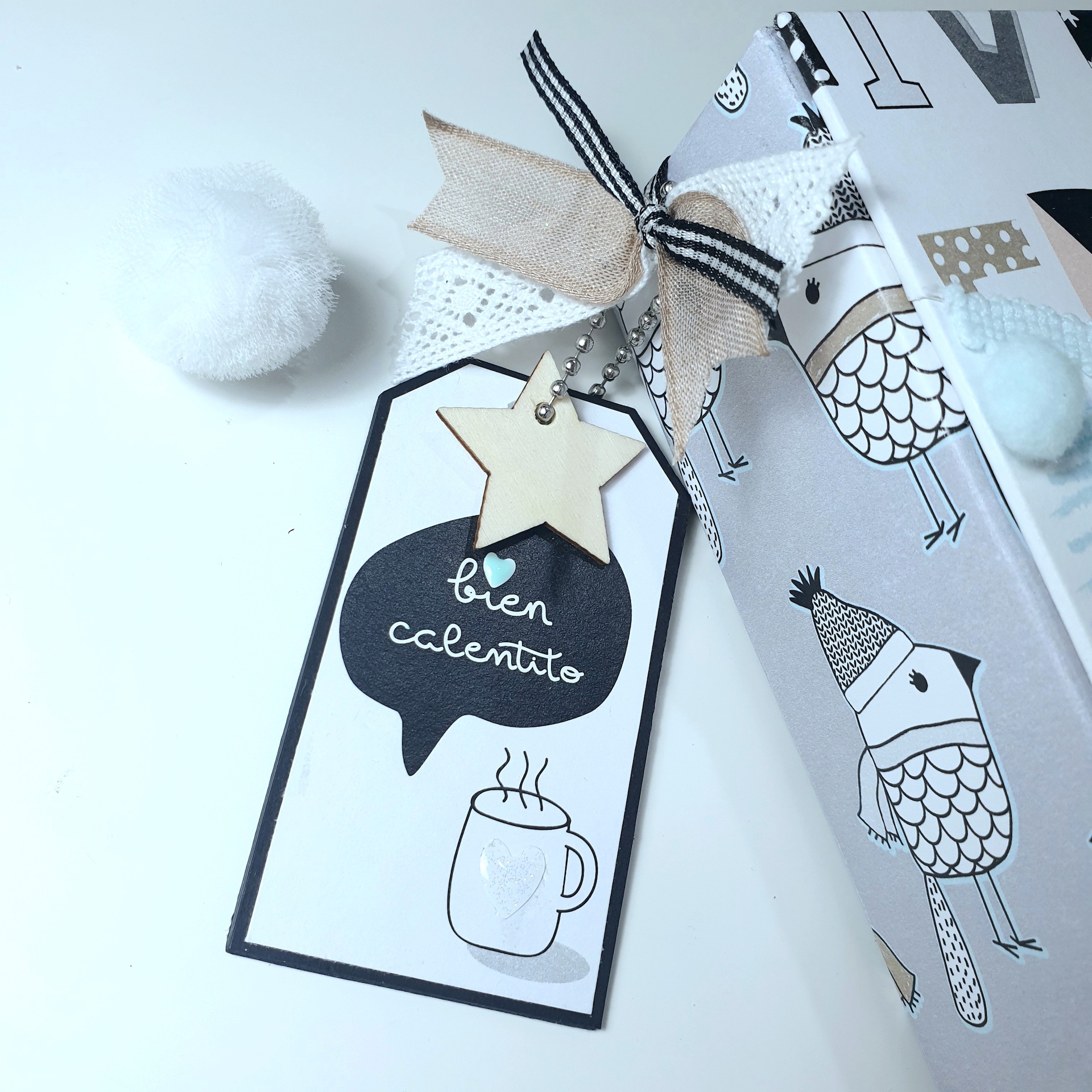 Etiqueta decorativa com texto 'bien caliente' e estrela de madeira junto a embalagem com padrão de pássaros.