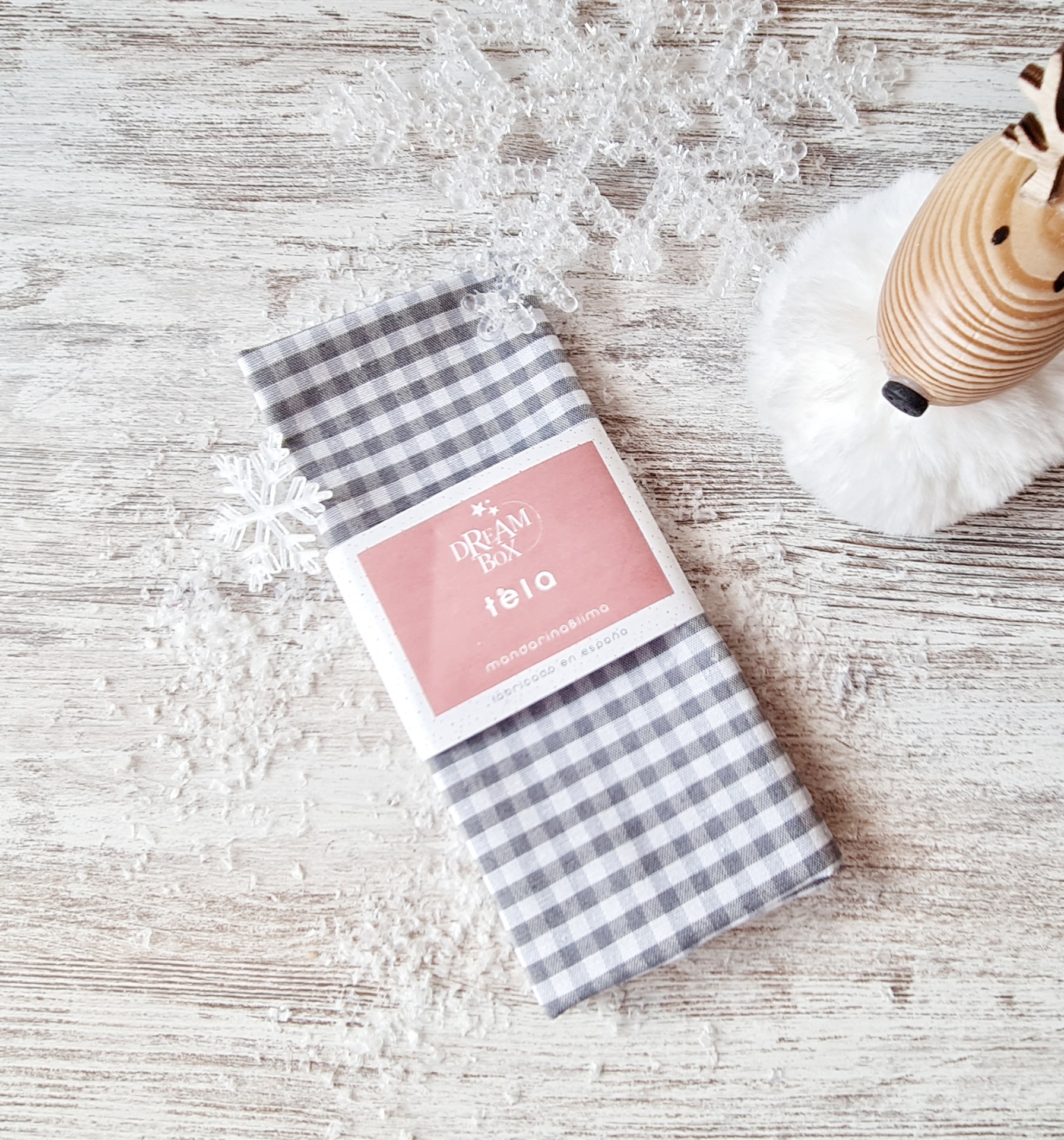 Guardanapo xadrez cinza e branco com etiqueta DREAM FOLIO num ambiente decorado com flocos de neve e rena de madeira