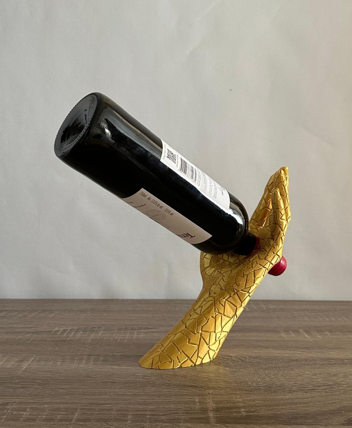 Porta-garrafa mão dourada segurando garrafa preta em superfície de madeira