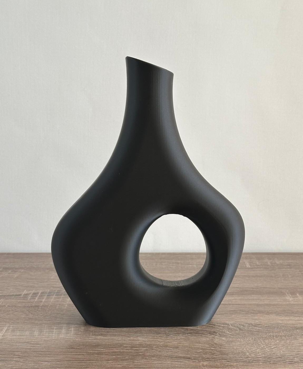 Vaso decorativo preto com forma arredondada e buraco central em superfície de madeira.
