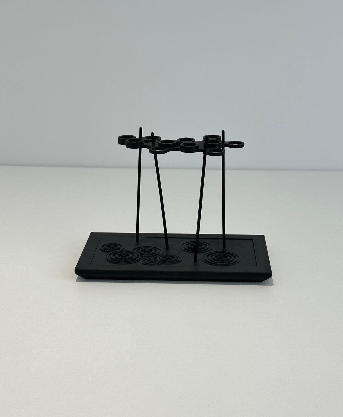 Suporte de metal preto com base retangular em fundo cinzento