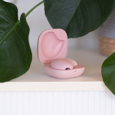 Estojo cor-de-rosa com auscultadores sem fios numa superfície branca com folhas verdes