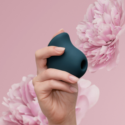 Dispositivo erotico azul escuro na mão com fundo rosa e flores cor-de-rosa