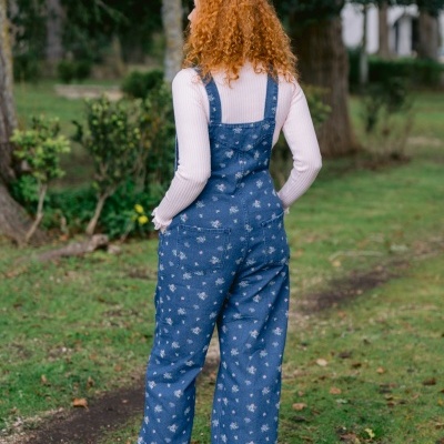 Pessoa de costas com jardineira de ganga azul floral, camisola rosa e ténis cinzentos em parque verde