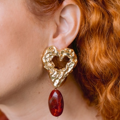 Brinco dourado em forma de coração com pendente vermelho em orelha.